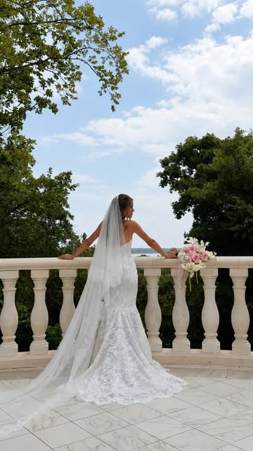 Bride in a lace gown holding a pink and white bouquet on a stone balcony