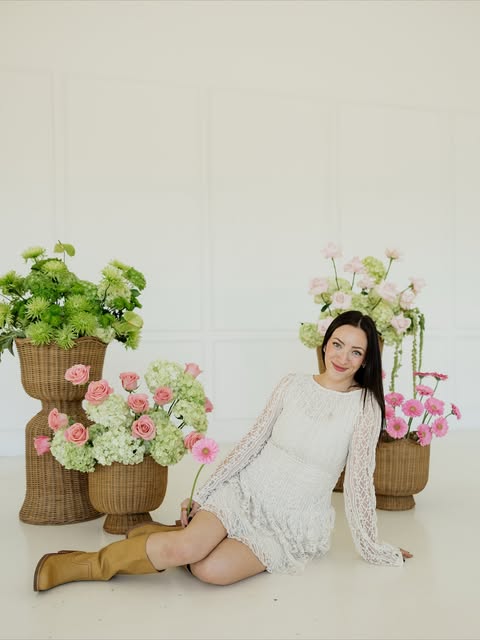Kayla, owner of Kay's Florals, seated among wicker baskets of pink and green flower arrangements